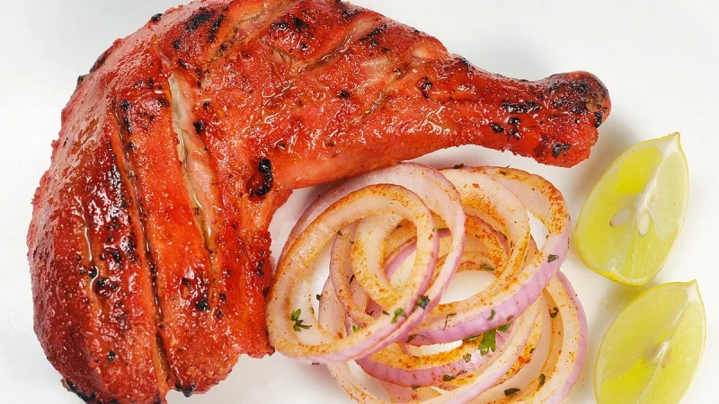 Tandoori chicken served with naan, mint chutney, and sliced onions on the side, emphasizing the dish's bold flavors and accompaniments.