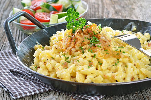 Tampilan dekat sepiring Spätzle dengan saus keju leleh dan taburan bawang goreng